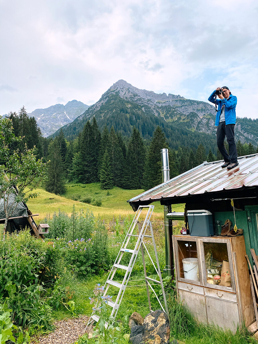 Fotograf Christopher Fuhrmann steht auf dem Dach einer Hütte im Kleinwalsertal und fotografiert mit der Kamera.
