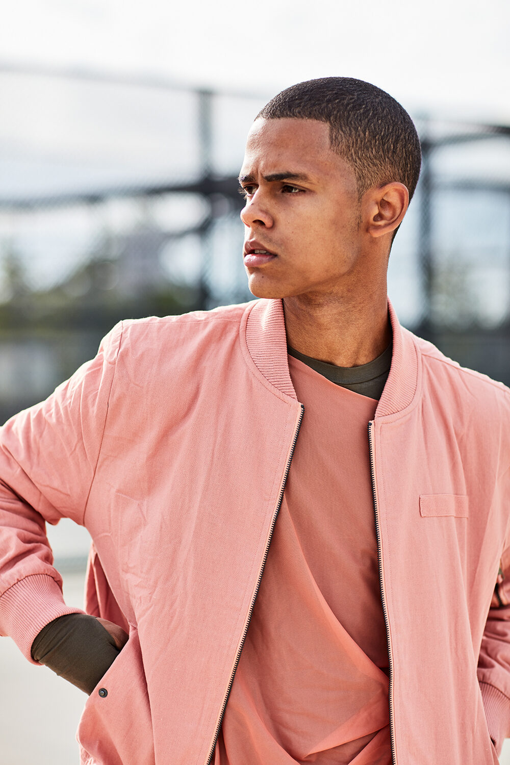 Color-Block-Editorial: Model David in rosa Bomberjacke über lachsfarbenem Shirt im urbanen Raum.