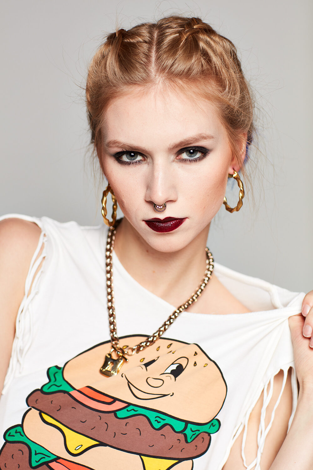 Beauty im Denim-Editorial: Model Maria mit dunklem Lippenstift und Septum-Ring in zerrissenem Burger-Print-Shirt.