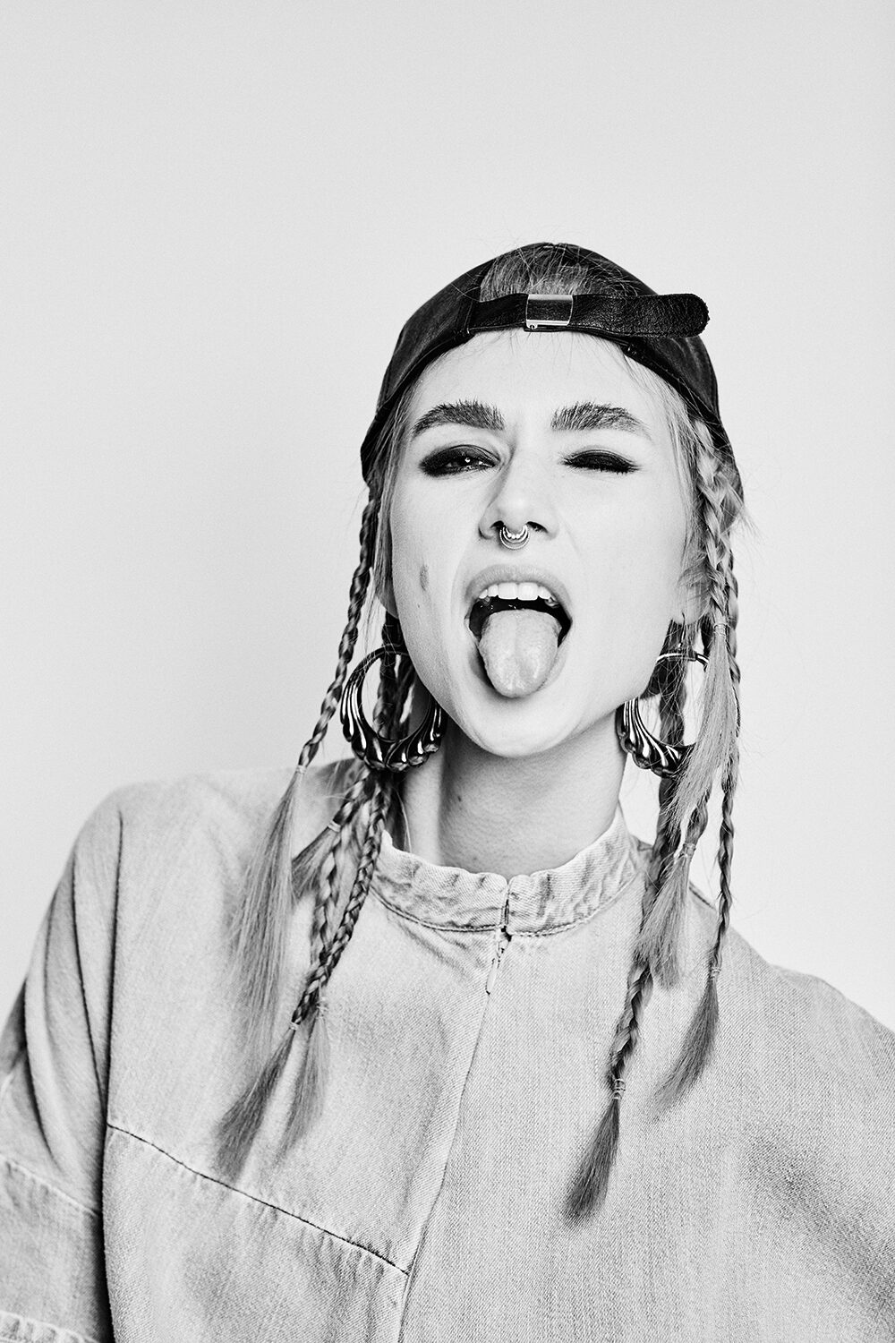 Schwarz-Weiß-Beauty im Denim-Editorial: Model Maria mit Cap und Zöpfen streckt die Zunge heraus.