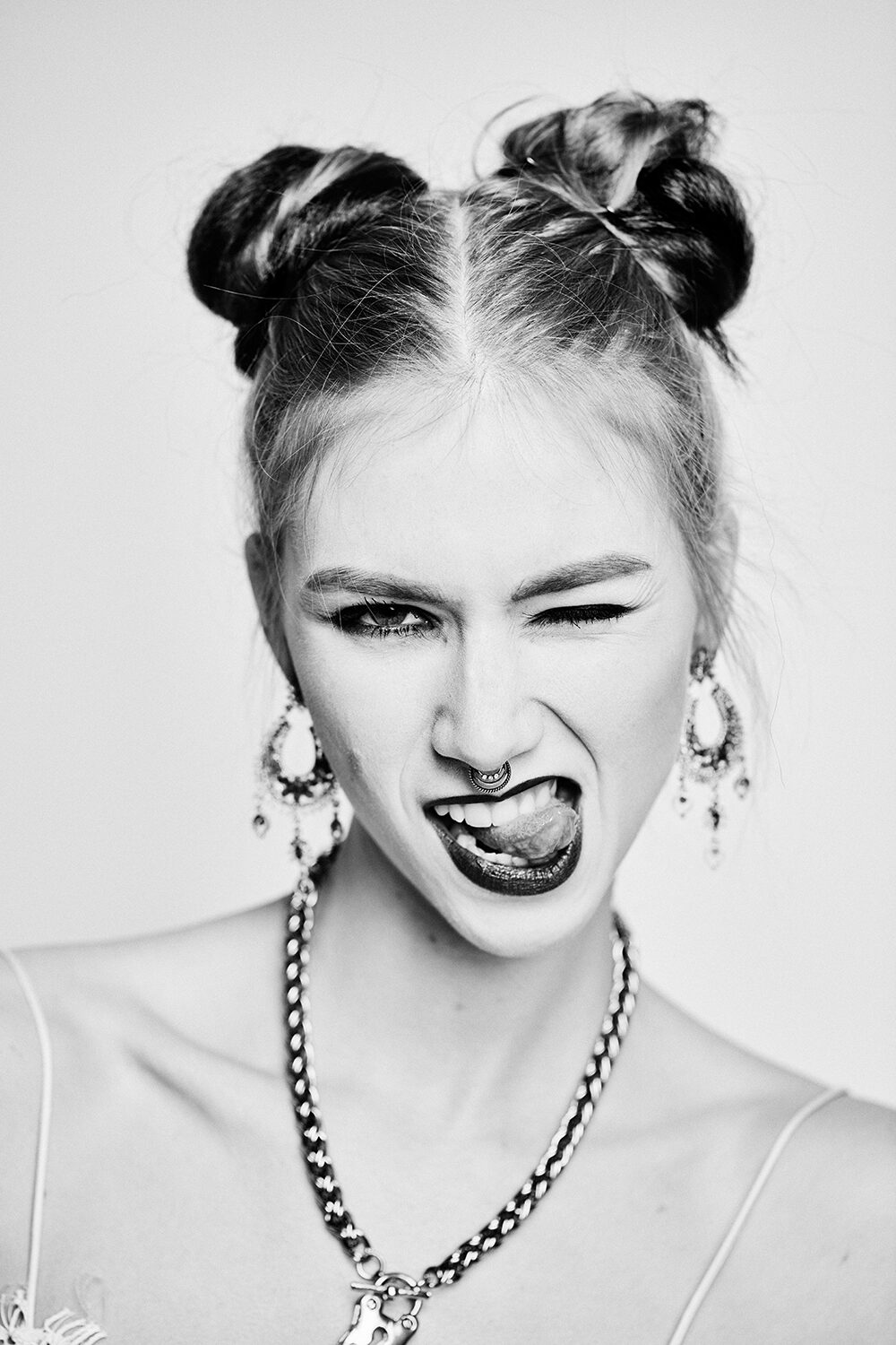 Schwarz-Weiß-Beauty-Editorial: blonde Frau mit Space Buns, auffälligen Ohrringen und dunklem Lippenstift.