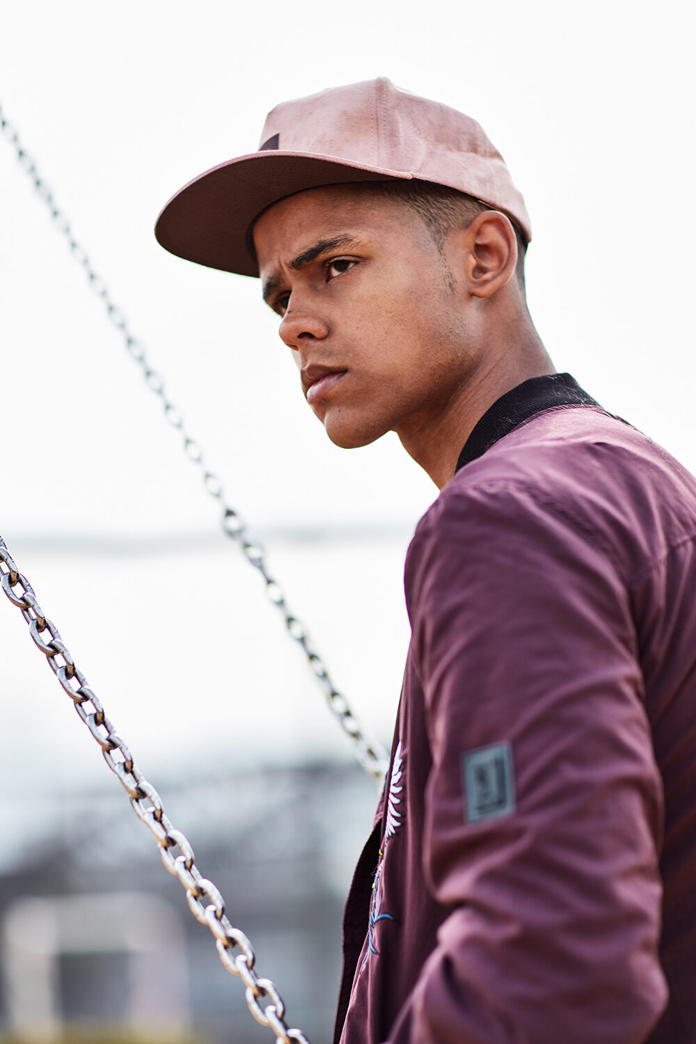 Streetwear-Editorial: Profilportrait eines männlichen Models mit rosa Cap und Bomberjacke im urbanen Raum.