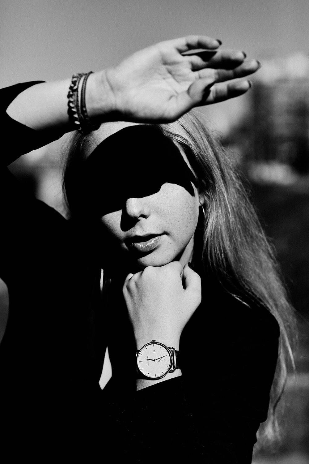 Schwarz-Weiß-Aufnahme: eine junge Frau schirmt die Augen mit der Hand ab, der Schatten fällt hart über ihr Gesicht.