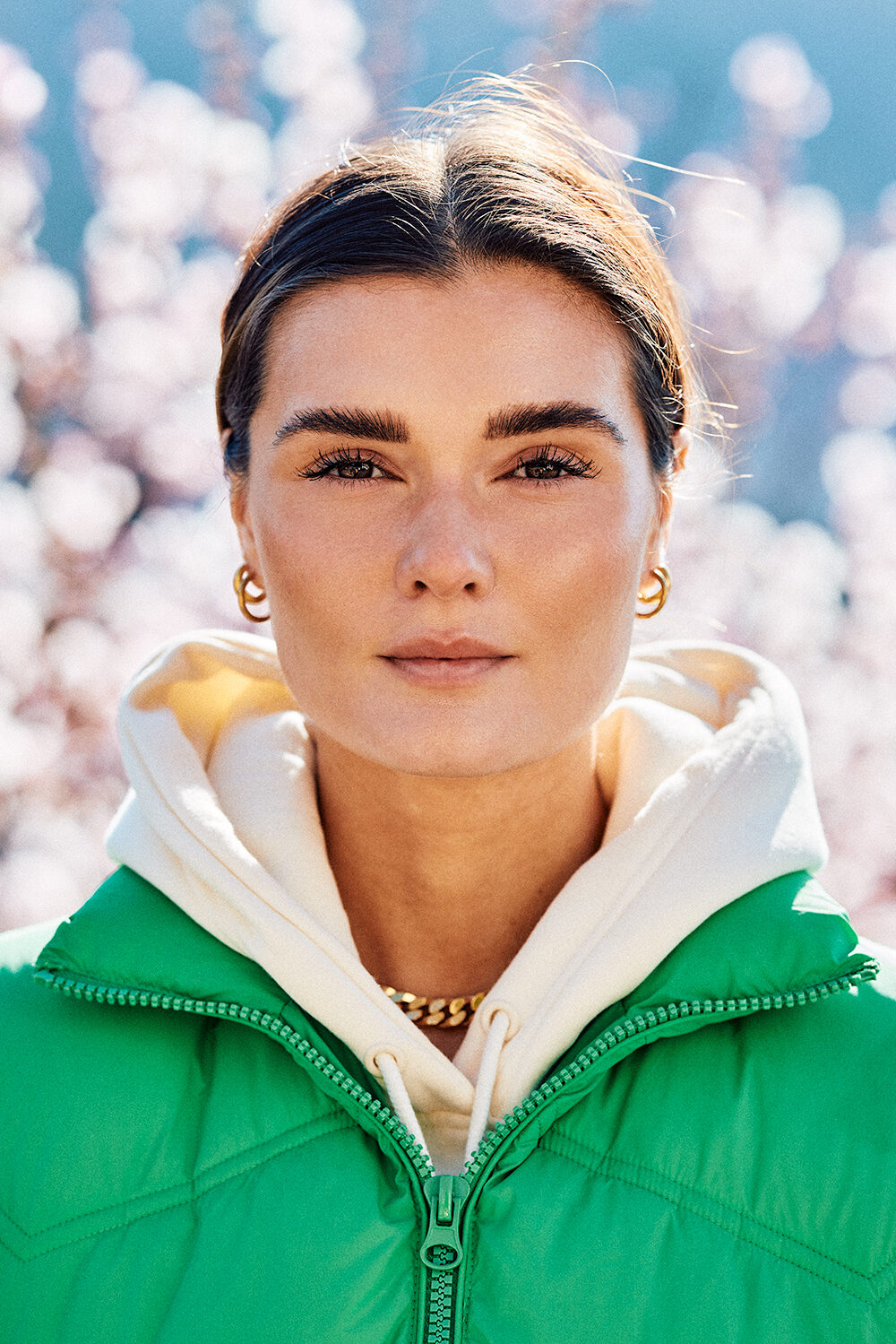 Beauty-Portrait der Fashion- und Lifestyle-Bloggerin Lea Endys in grüner Steppjacke vor blühenden Kirschblüten in Heidelberg.