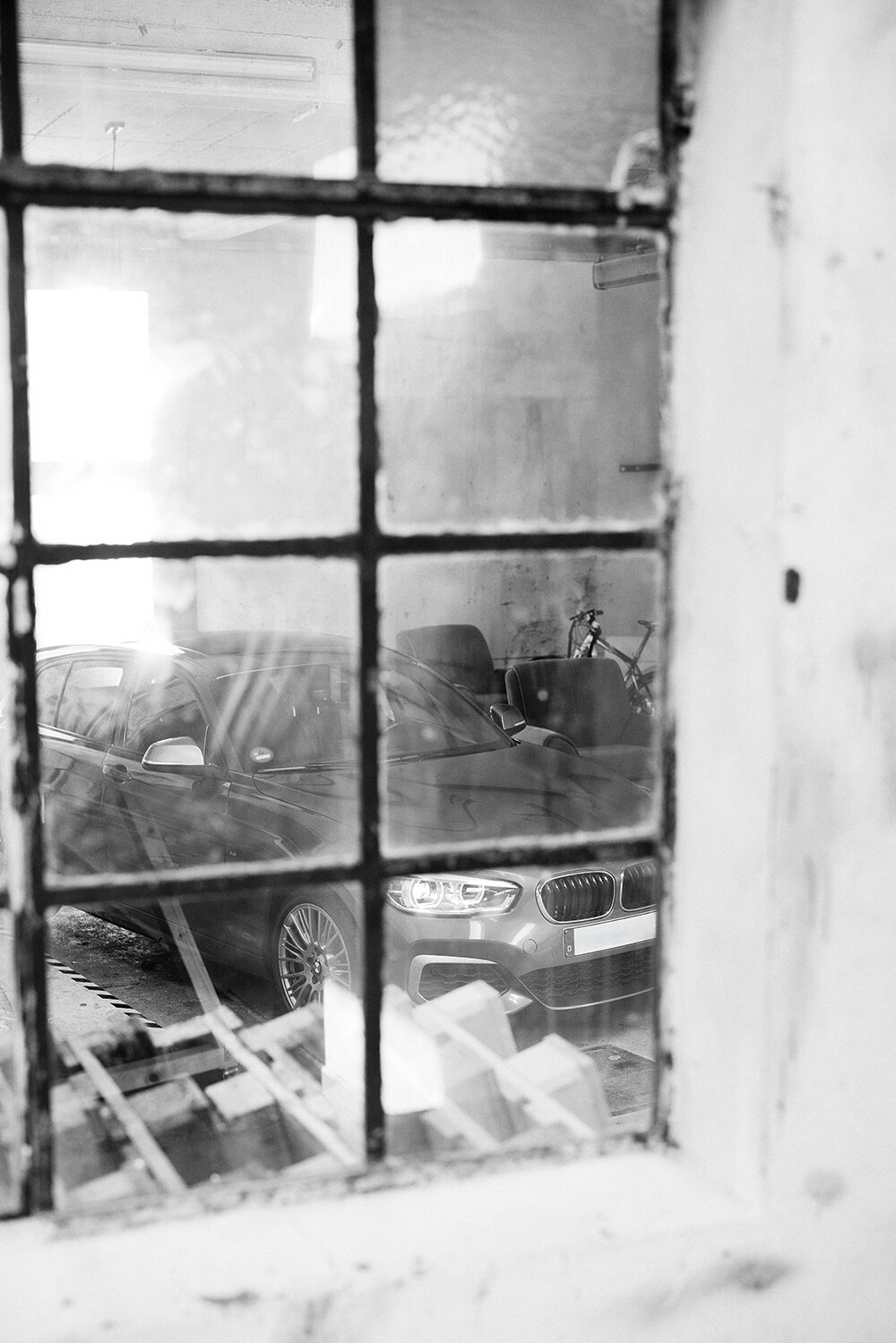 Schwarz-Weiß-Aufnahme eines BMW M140i xDrive, fotografiert durch ein altes Sprossenfenster, in der Einfahrt des Schärferaums in Bad Homburg.