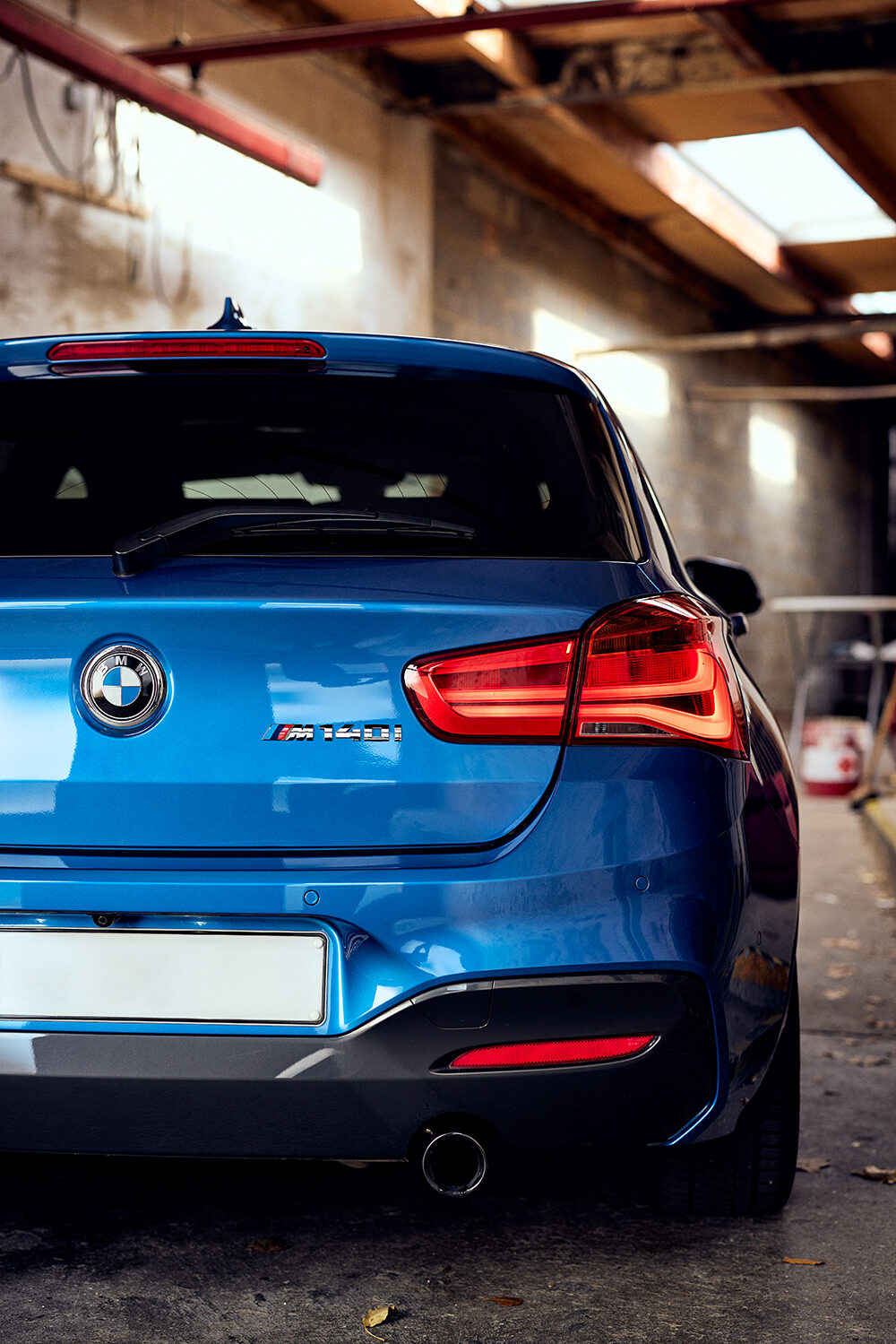 Heckansicht eines estorilblauen BMW M140i xDrive in der Halle des Schärferaums in Bad Homburg.