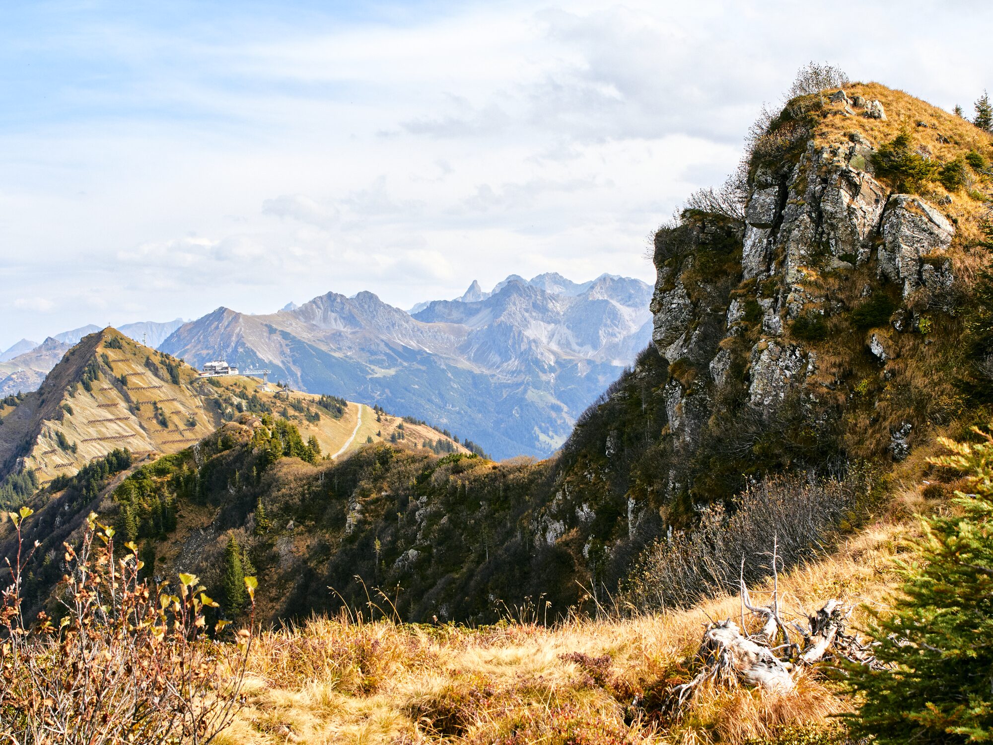 Herbstlich gefärbte Grasberge im Kleinwalsertal mit Blick zum Walmendingerhorn und seiner Bergstation, dahinter die felsigen Gipfel der Allgäuer Alpen.