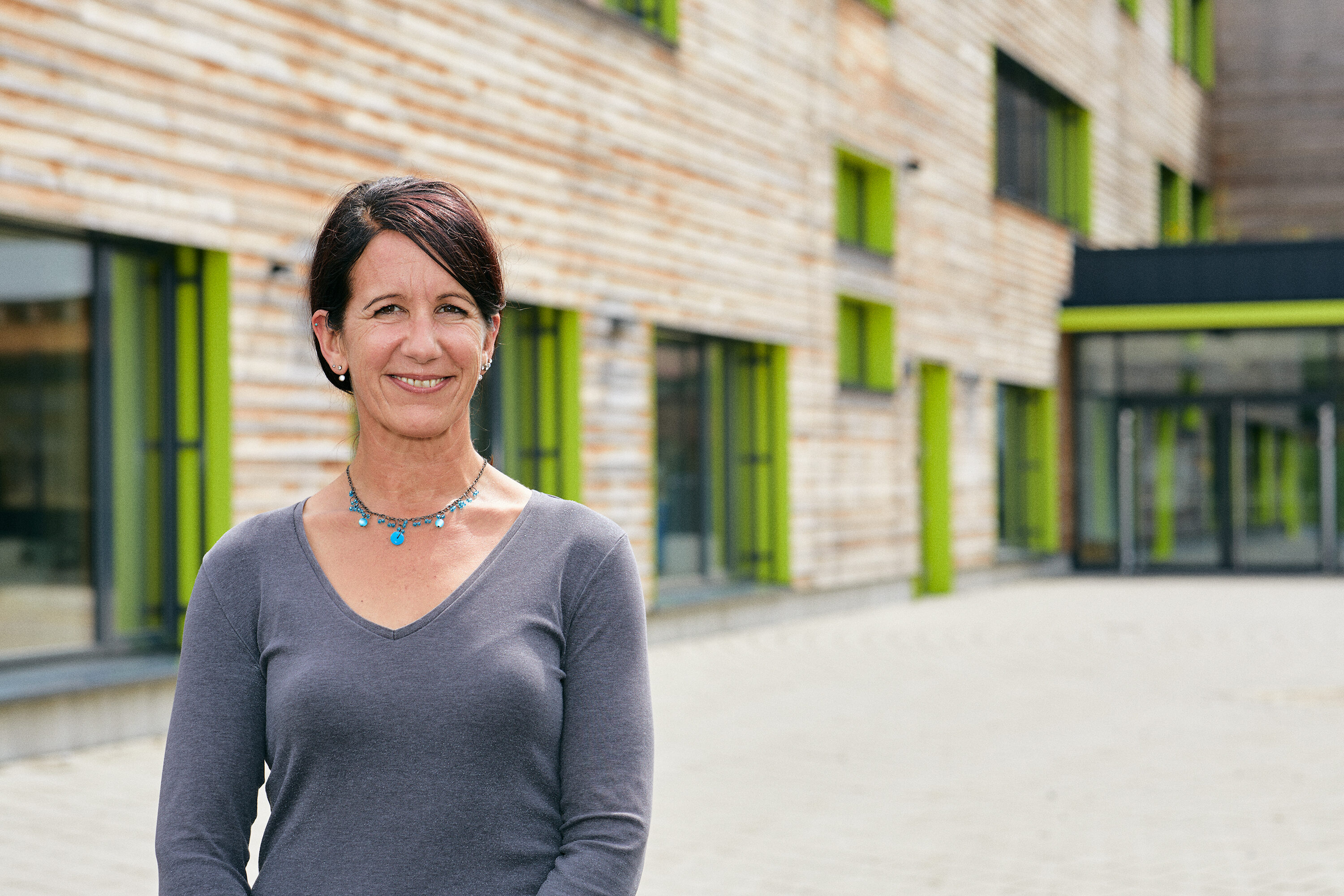 Eliane Fritz steht lächelnd vor dem modernen Holzbau des Schulzentrums Kleinwalsertal.