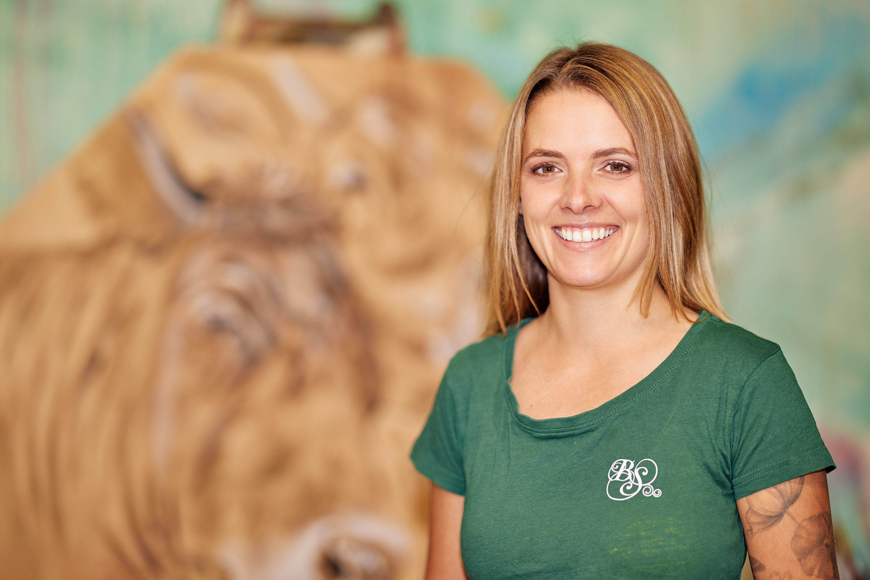 Künstlerin Bianca Schneider im grünen Shirt vor einem ihrer gemalten Bilder mit Rinderkopf im Kleinwalsertal.