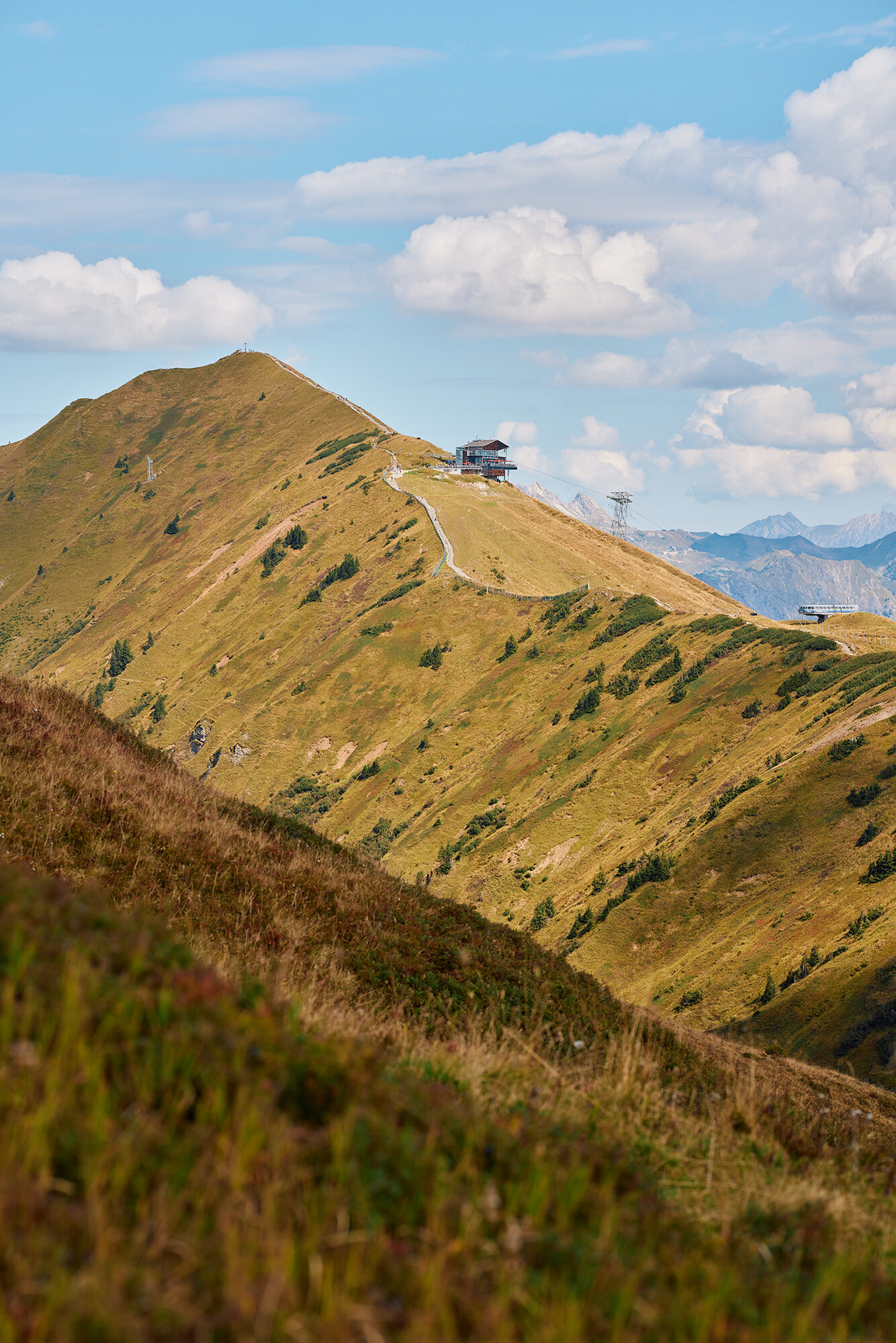 Berggipfel mit Bergstation im Kleinwalsertal unter blauem Himmel mit Schäfchenwolken.