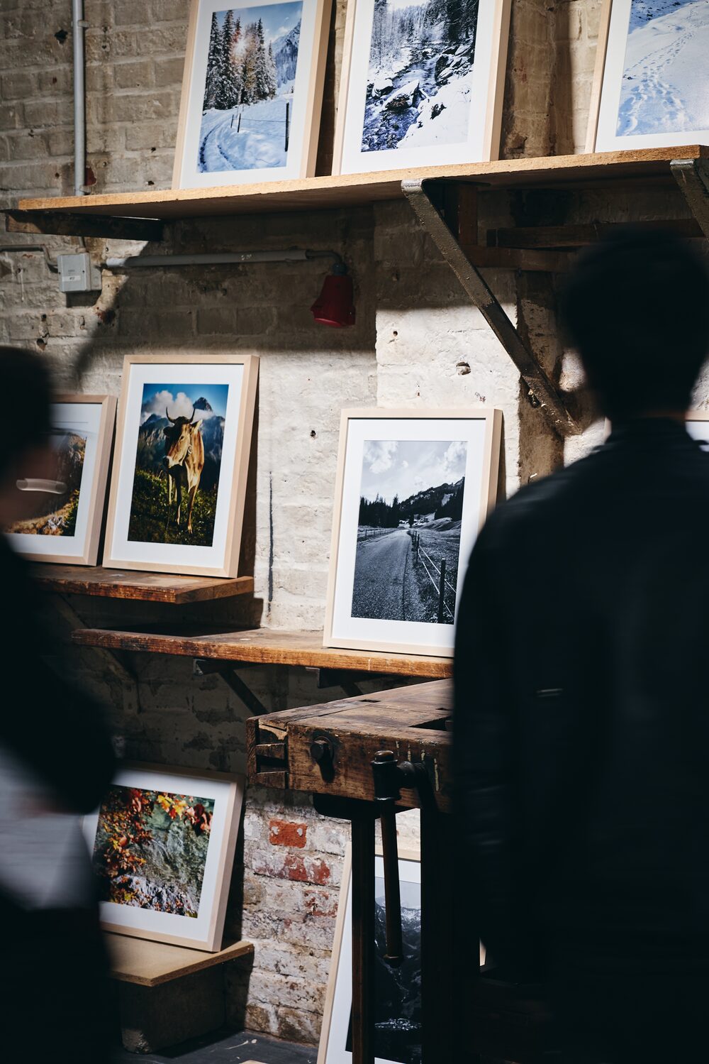 Besucher betrachten gerahmte Bilder der Ausstellung Walser Stories auf Holzregalen im Schärferaum in Bad Homburg.